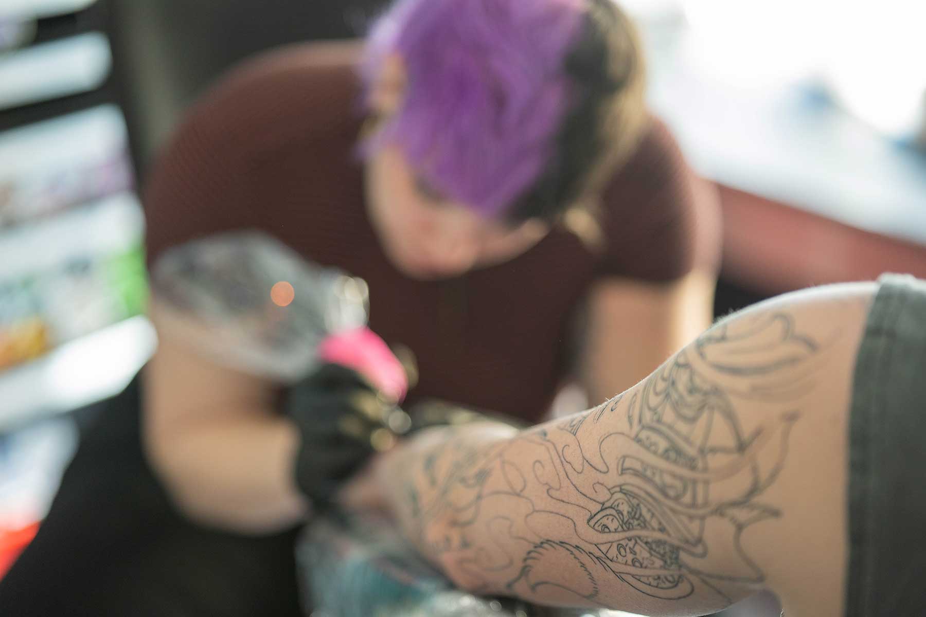 Tattoo artist working on a detailed arm design.