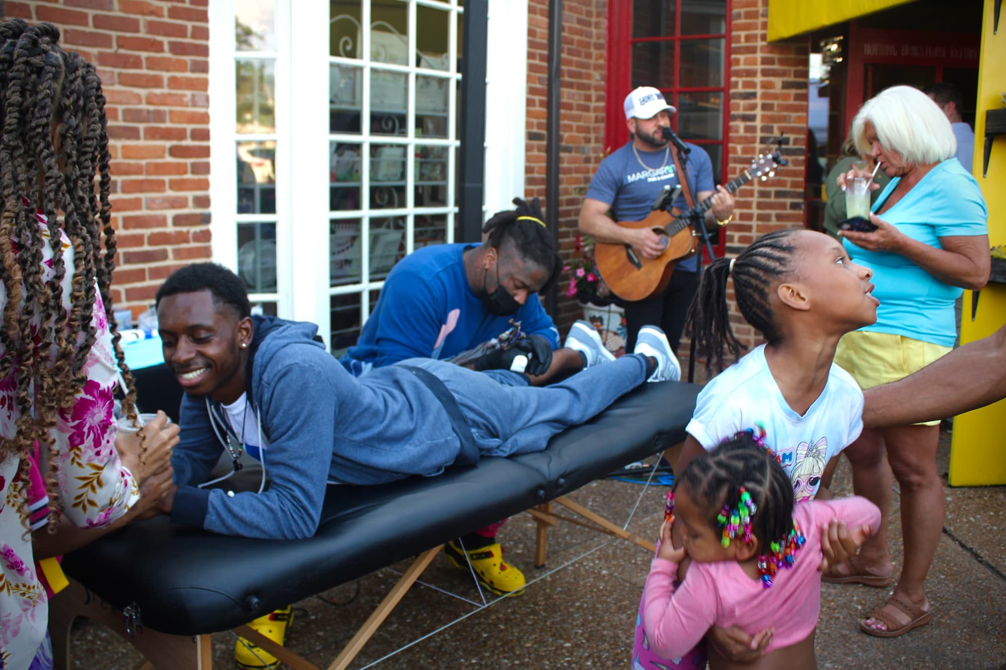 Outdoor tattoo session with musician and audience interaction.