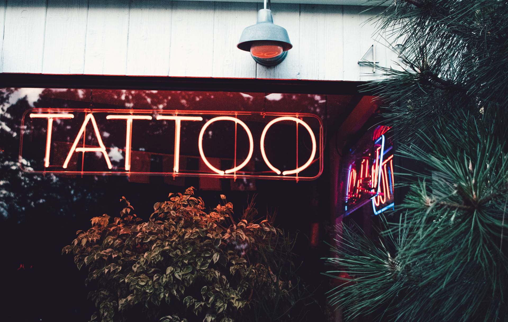 Glowing red neon "Tattoo" sign mounted on a tattoo shop storefront at dusk, illustrating how to choose the best tattoo shop in St. Louis