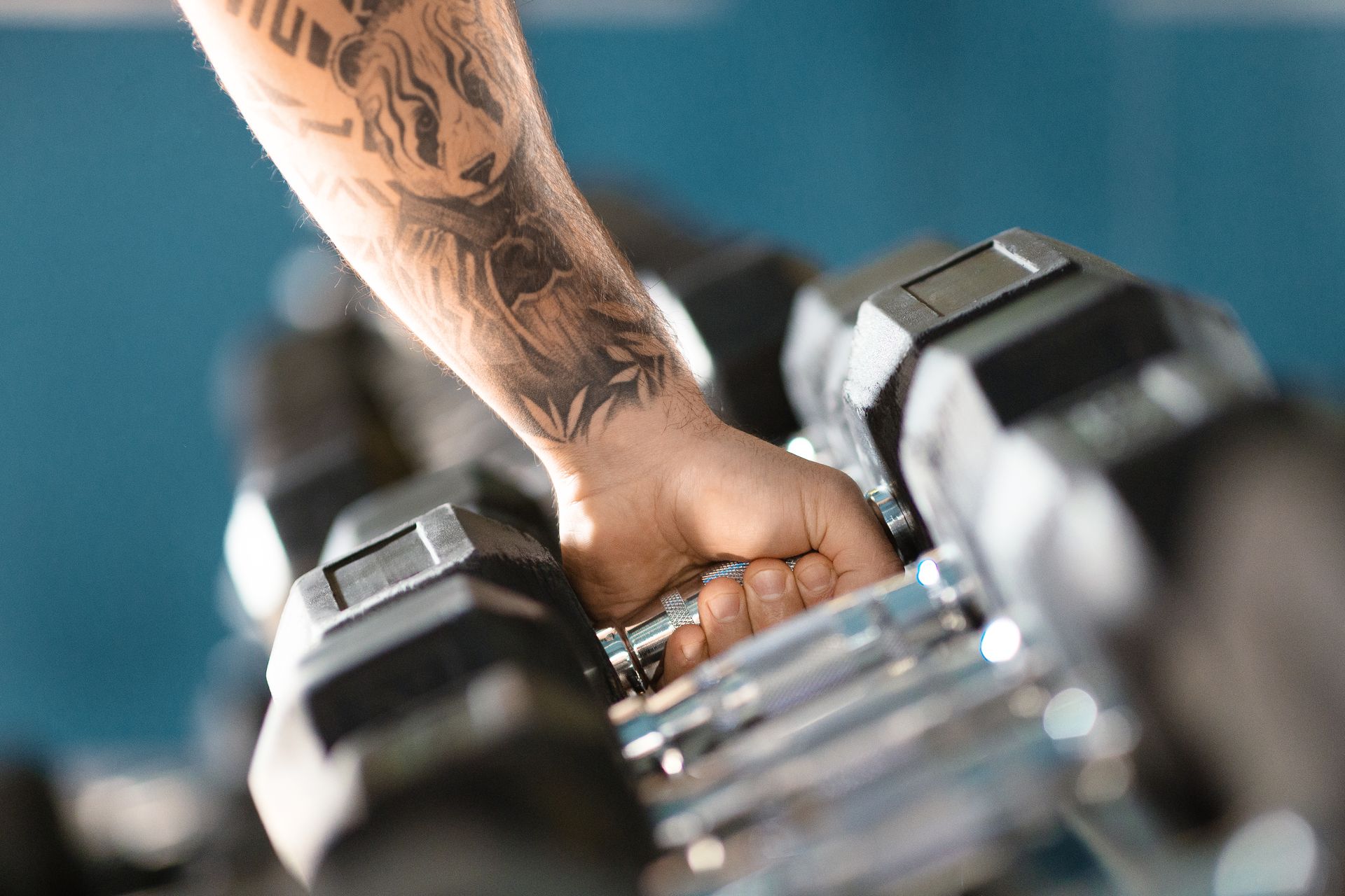 Man with a tattooed forearm gripping a dumbbell from a gym rack while working out after a tattoo