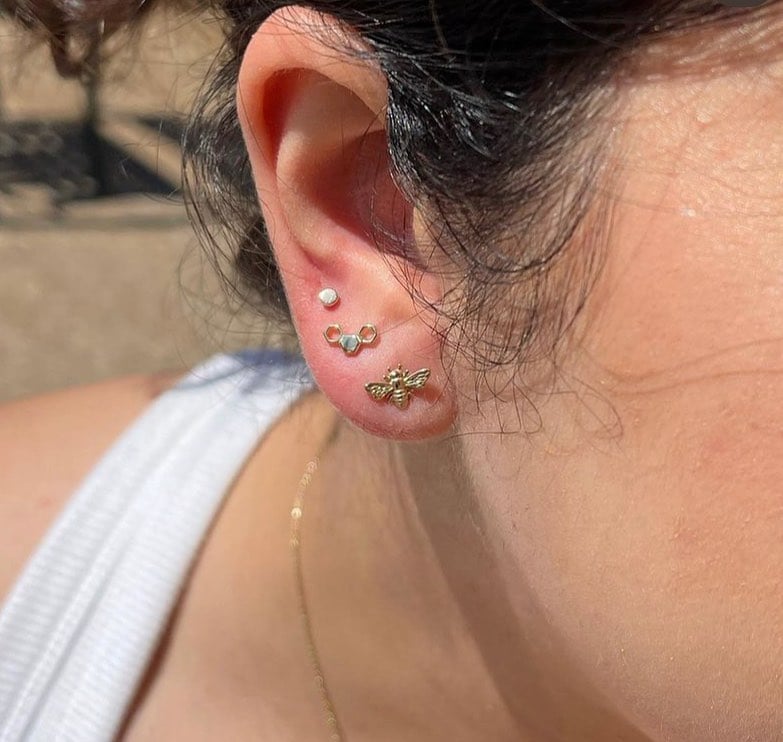 Stacked lobe piercings with gold bee and flower studs done at Enigma Tattoos