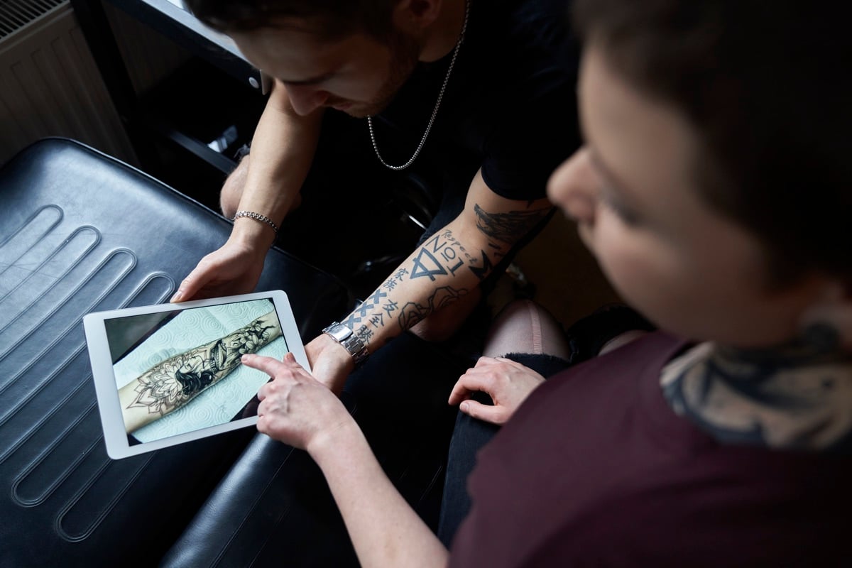 Tattoo artist showing a client a design on a tablet during a consultation